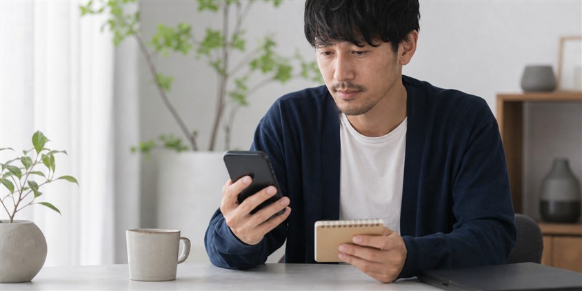 ヒゲ脱毛のプランをスマートフォンと手帳で比較する男性