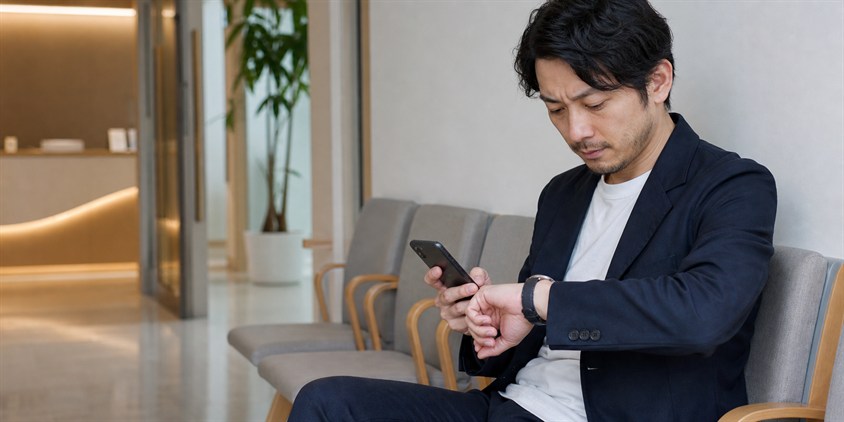 クリニックの待合室で予約時刻を確認する男性